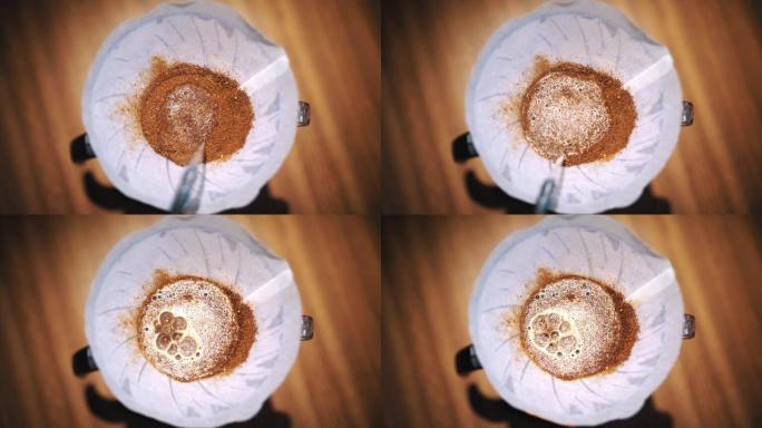滴咖啡冲泡。特写。咖啡师在传统的滴灌冲泡设备中，将专用水壶中的沸水倒在新鲜磨碎的咖啡豆中