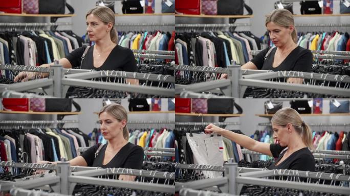 一家小服装店的女人选择挂在衣架上的时髦衣服。她反思并评估所提供服装系列的质量。在折扣时间去购物。