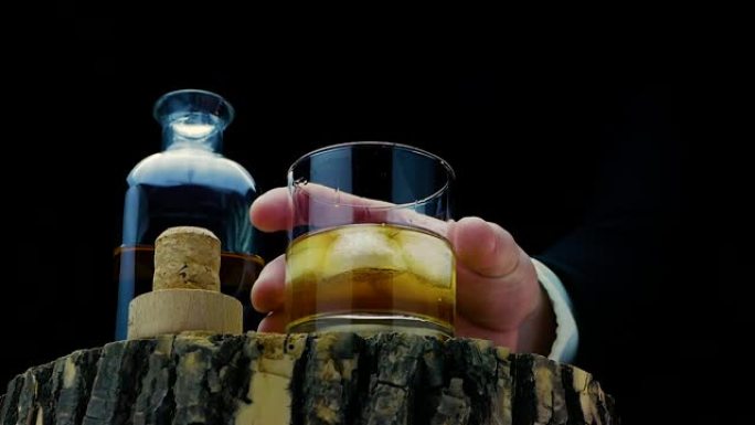 在木架上喝威士忌，在冰上喝一杯威士忌。一名男子在黑色背景上喝威士忌的慢动作镜头