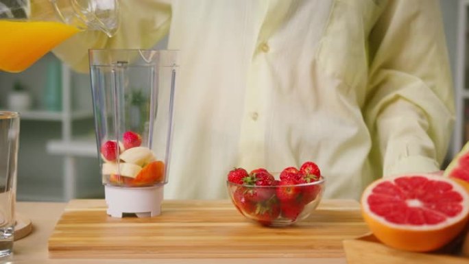 女人将成熟的草莓放入带有切好的苹果和香蕉特写镜头的搅拌机中，倒入橙汁，煮冰沙，不含糖的健康甜鸡尾酒。