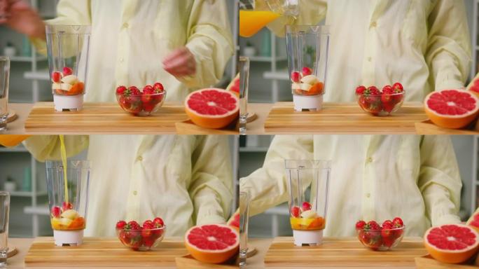 女人将成熟的草莓放入带有切好的苹果和香蕉特写镜头的搅拌机中，倒入橙汁，煮冰沙，不含糖的健康甜鸡尾酒。