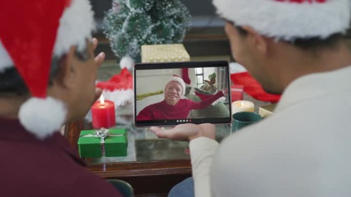 混血儿的父亲与儿子挥舞着，并使用平板电脑与屏幕上的男人进行圣诞节视频通话