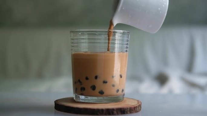 在玻璃杯中倒入带有木薯珍珠泡沫的泰国奶茶。慢动作
