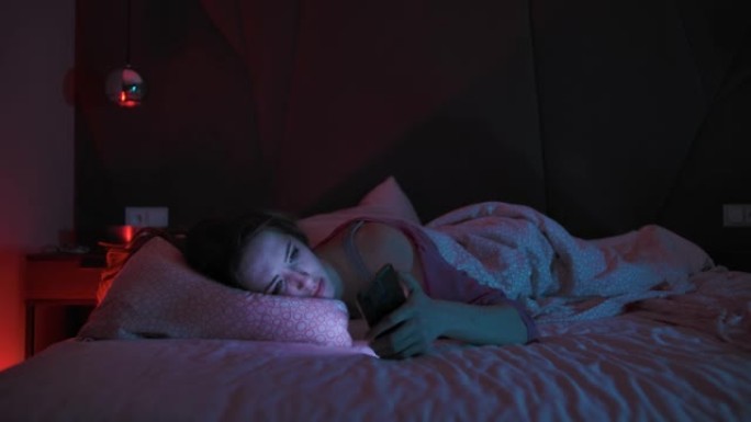 年轻女子难以入睡检查手机一个年轻女子晚上躺在床上