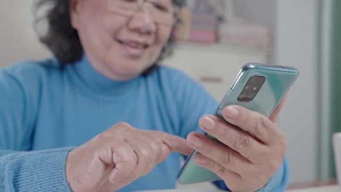 特写亚洲老妇使用智能手机，穿毛衣在家保暖，老年人视力快乐退休生活，现代科技移动应用，积极态度模特微笑