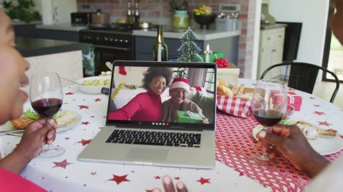 非裔美国人夫妇与葡萄酒使用笔记本电脑与家人在屏幕上进行圣诞节视频通话