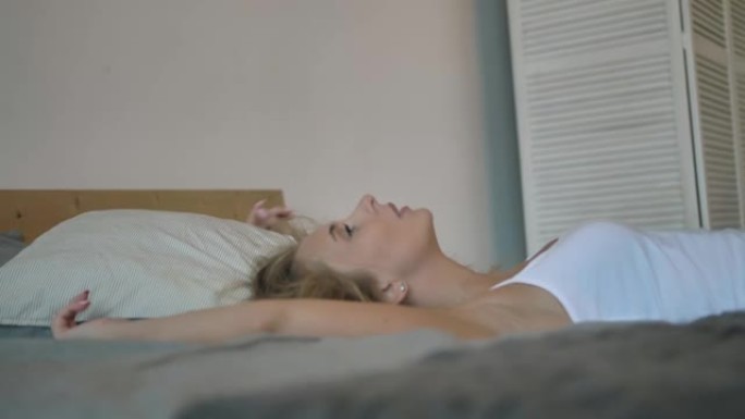 性感的女孩穿着白色背心和蓝色牛仔短裤躺在床上