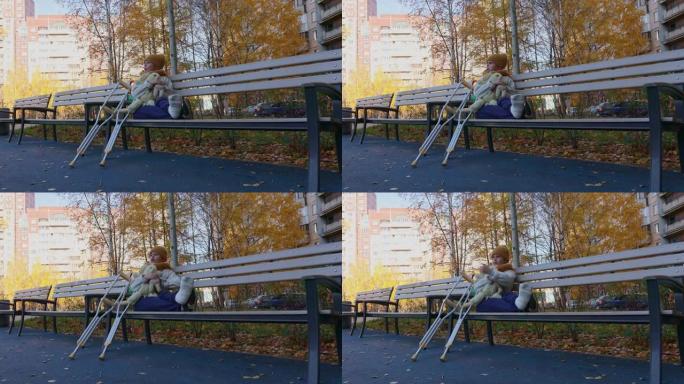 孩子拄着拐杖在秋季公园散步。坐在公园长椅上玩玩具的孩子。女孩的一条腿骨折了。