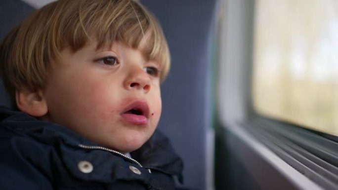 沉思的小男孩在旅途中看着火车窗外，看到乡村经过