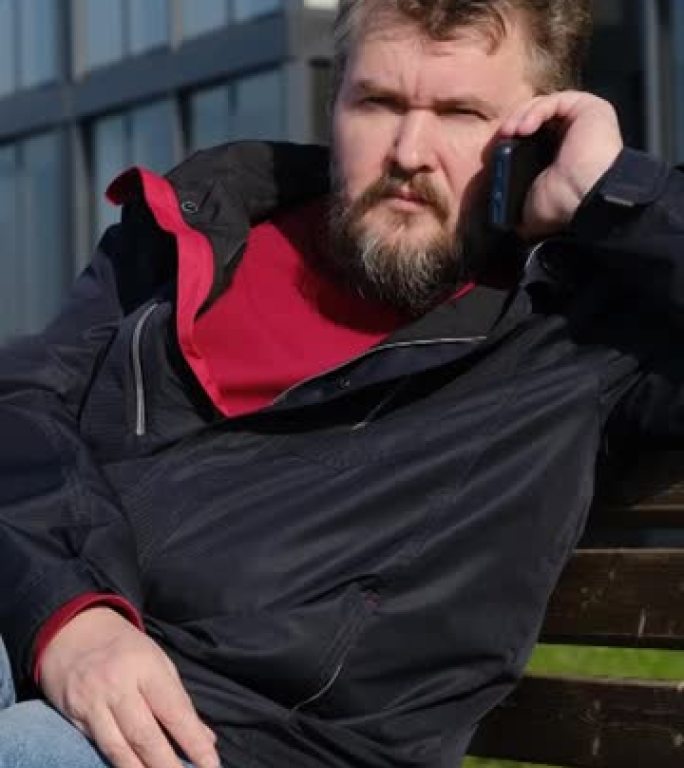 成熟的男人坐在长凳上使用电话