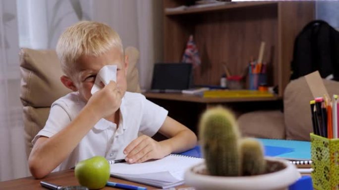 一个小男孩正在做作业，他感冒了，用餐巾纸擦鼻子。