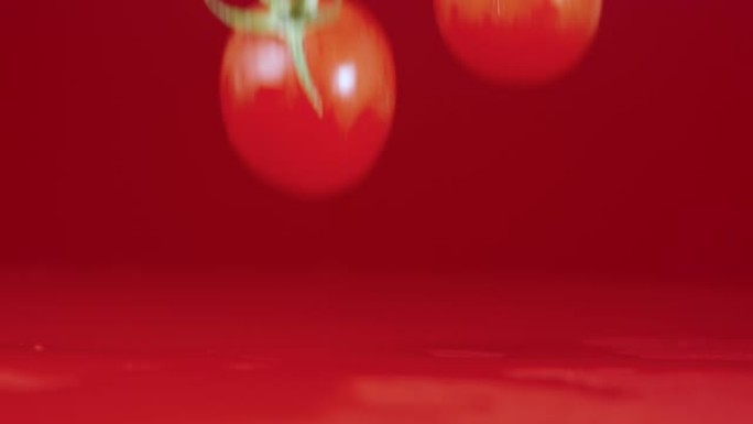 一组红色成熟西红柿的视频镜头，绿色尾巴落在潮湿的反光桌面上。成熟的樱桃在红色工作室背景上泼水击中桌子
