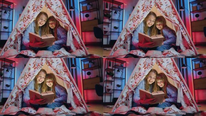 关闭可爱的快乐友好的两个不同年龄的姐妹，他们在家里度过了共同的休闲时光，晚上在令人惊叹的装饰帐篷里看