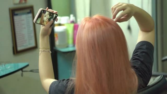 年轻女子在美容院垂死头发，使用智能手机进行自拍