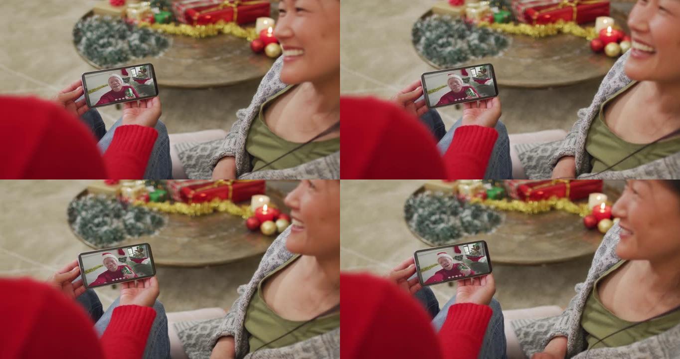微笑的亚洲夫妇使用智能手机与屏幕上戴着圣诞老人帽子的男人进行圣诞节视频通话