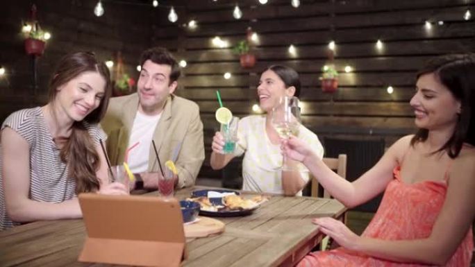 在餐厅里，一群现代而快乐的男女朋友在视频通话中与鸡尾酒一起敬酒