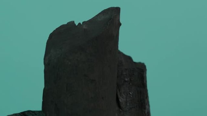 木炭。蓝绿色屏幕背景上的黑色木炭。用于烹饪烤架或工业。天然木炭。通过强烈加热木材产生的黑碳。烧烤。