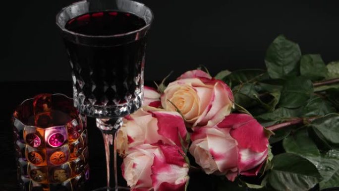 玫瑰花在水晶酒杯附近，红酒和燃烧的candele，黑色背景