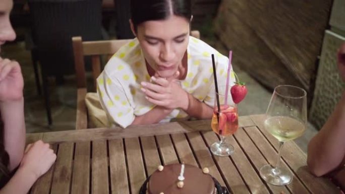 在与女性朋友庆祝时，快乐的女人在生日蛋糕上吹蜡烛时许愿