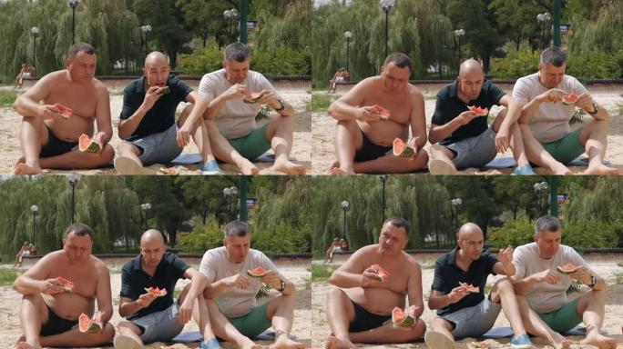 一群朋友在夏天吃西瓜的野餐时间。三个男性朋友非常有魅力和可爱坐在草地上野餐。慢动作