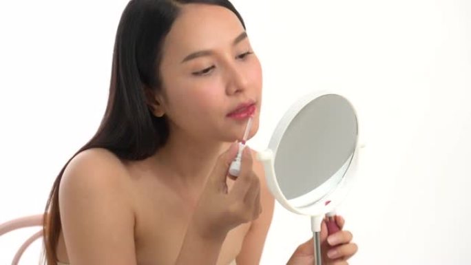 喜欢化妆的亚洲女人。年轻迷人美丽的感觉快乐的样子镜子和脸上的眉毛着色享受白色背景上的美容化妆品