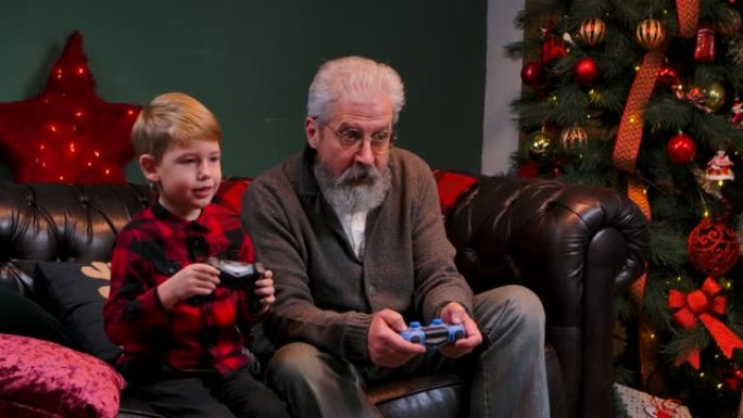快乐的老爷爷和孙子用操纵杆玩游戏。优雅的白发男子和一个小男孩坐在一个装饰的房间里的沙发上，靠近一棵发