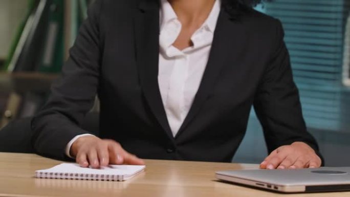 非裔美国妇女的肖像坐在桌子旁，打开笔记本电脑，开始工作。女商人在办公室内部的工作场所摆姿势。特写。慢