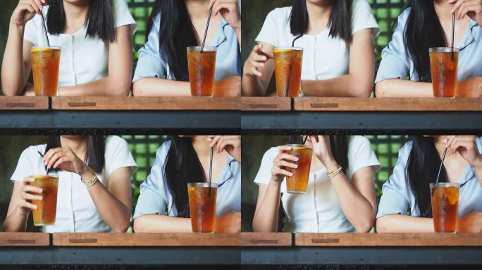 在咖啡馆用吸管用塑料杯喝冰茶的妇女的特写镜头。