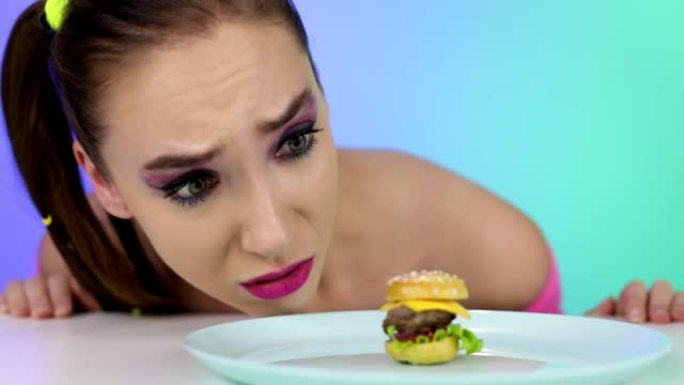 素颜的心烦意乱的女孩看着一个小汉堡。