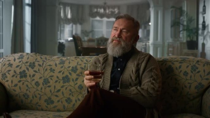 老商人坐在沙发上喝威士忌杯。肖像高级绅士