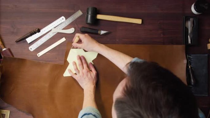 用模板和锋利的特殊刀定制切割牛棕色皮革。工作场所桌子上的牛皮，制作由真皮或人造革制成的手工产品