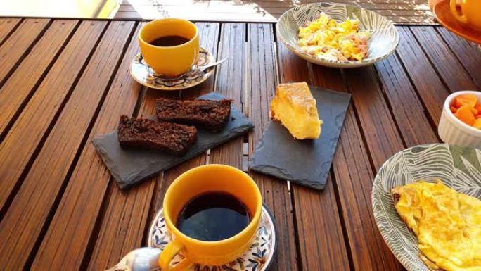 女人提供丰盛的早餐桌，炒鸡蛋加火腿，饼干和香蕉蛋糕，木瓜，咖啡，牛奶加咖啡和草莓酱。