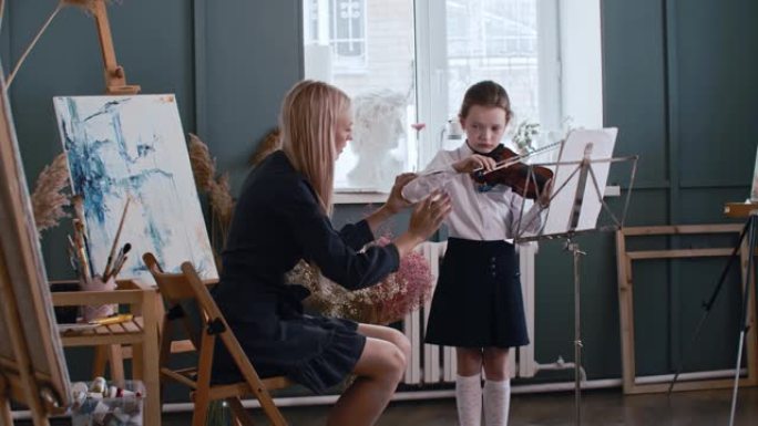 年轻的金发女老师教小女孩如何在拉小提琴课时正确握弓
