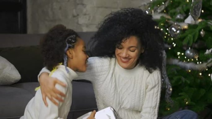 非裔美国妈妈的肖像给她的小女儿带来了礼物。女人和女孩坐在沙发和装饰圣诞树附近。家庭之夜快乐。特写。慢