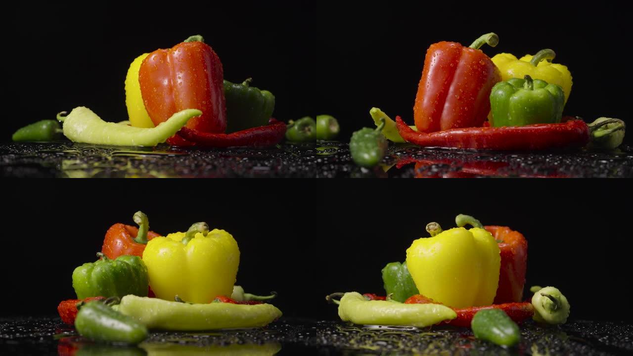 黑色背景上滴着湿气的胡椒。红色，绿色和黄色的辣椒，墨西哥胡椒和甜椒被水滴覆盖。特写。慢动作就绪，4k