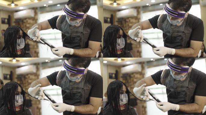 剪掉女性客户头发时戴着口罩和盾牌的男性理发师