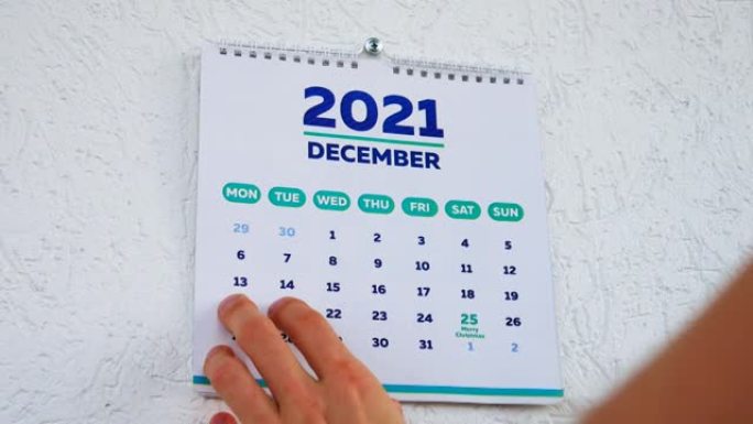 男性手的特写镜头撕下了挂历2021的11月页，并用手指指着12月页上的圣诞节日期