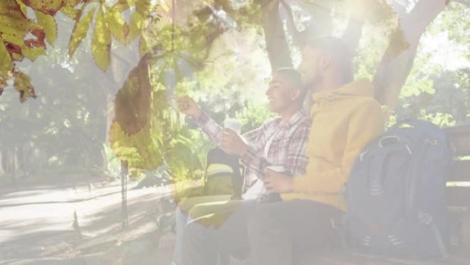 快乐的混血男性朋友在长凳上聊天，阳光照在树叶上的合成