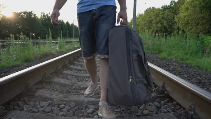 男子缓慢地沿着铁路铁轨行走，手里拿着路包