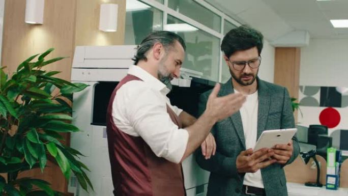 一位英俊的大胡子老板正在办公室用平板电脑帮助他的一名工人