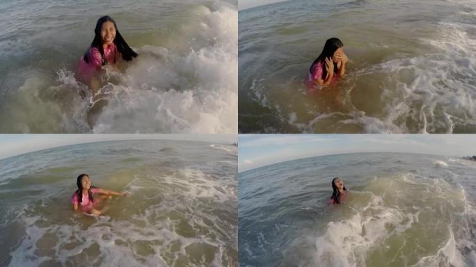 穿着粉红色泳衣的快乐亚洲女孩和她的兄弟在度假期间一起在海滩上享受海浪。