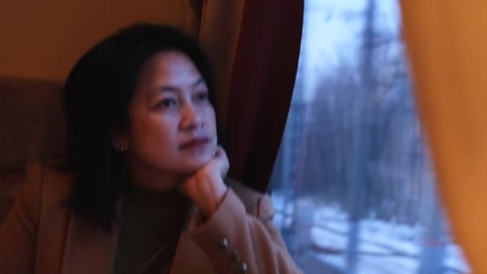 亚洲妇女穿着棕色外套独自乘火车旅行，透过窗户看风景