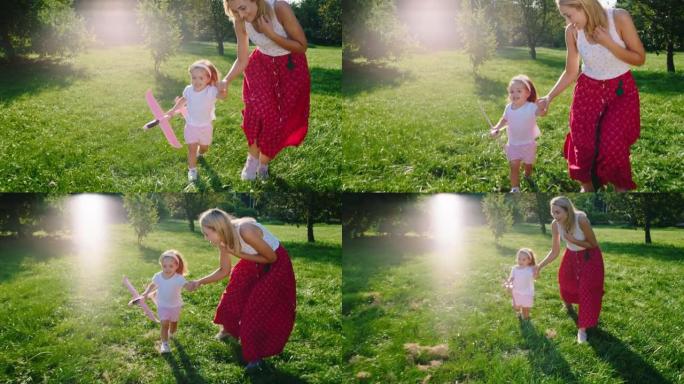 快乐而兴奋的妈妈和她的小女儿在镜头前奔跑，手里拿着飞机穿过草地。在阿里·阿列克谢迷你上拍摄。