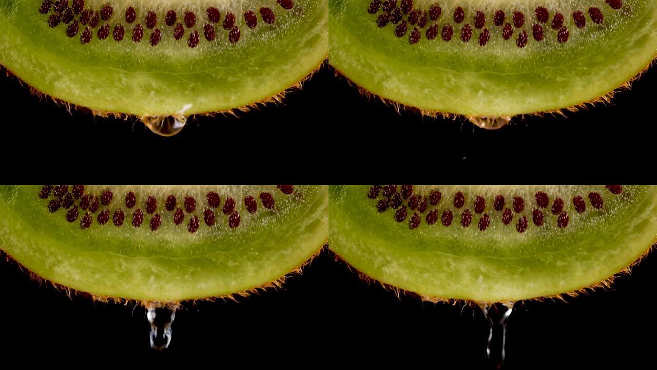 微距滴水滴落的新鲜绿色猕猴桃切片和黑色背景上的种子果实。慢动作水滴从多汁的新鲜成熟美味切片猕猴桃，特