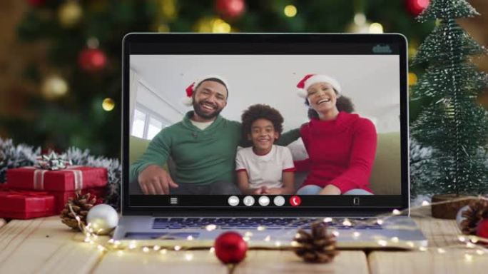 在笔记本电脑视频通话中戴着圣诞老人帽子的快乐家庭，带有圣诞节装饰品和树木