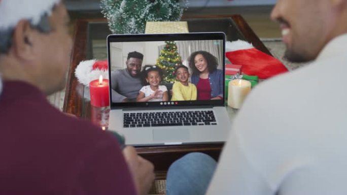 微笑的混血儿父亲和儿子使用笔记本电脑与家人在屏幕上进行圣诞节视频通话