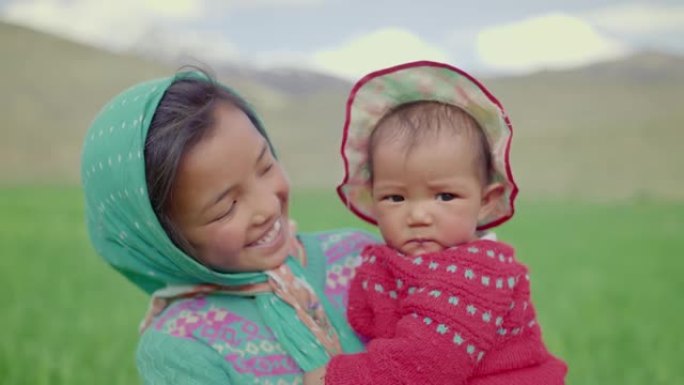 年轻的农村小女孩抱着一个可爱的婴儿女婴姐姐站在山区的农业田里