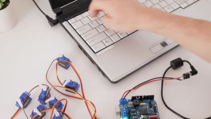男性程序员创建机器人技术，一个开源硬件和软件板控制伺服电机。DIY机械师，通过笔记本电脑上的代码编程