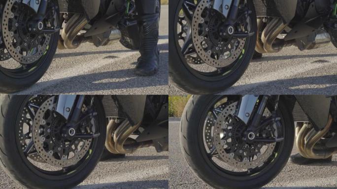 停在乡间小路上准备骑行的运动型摩托车前轮的特写。穿着摩托车防护靴的男性摩托车手将驾驶摩托车。冒险的概
