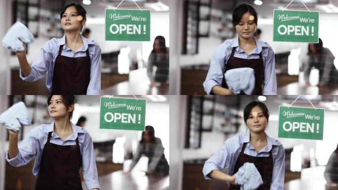 中式风格的年轻女性咖啡店老板用衣服擦拭和清洁咖啡馆前门的透明玻璃墙，然后打开为客户服务，背景是团队清
